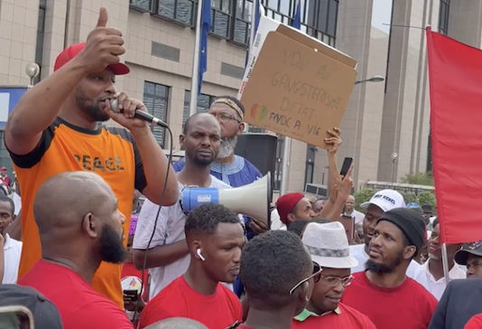 Feature image Djanii Alpha s'exprimant devant des partisans du FNDC à Bruxelles