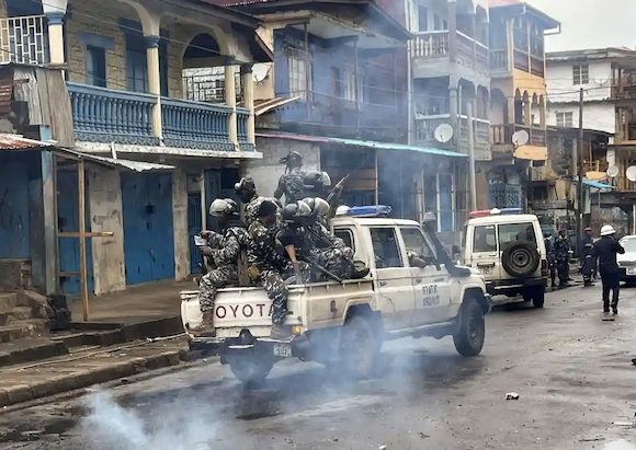 La police anti-émeute patrouille en passant devant la fumée qui s'élève d'un barrage routier lors de manifestations anti-gouvernementales à Freetown, en Sierra Leone. Photographie : Umaru Fofana/Reuters